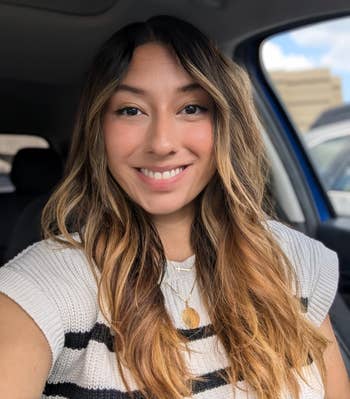 Reviewer successful a car smiling, wearing a knitted apical with achromatic stripes and layered necklaces, looking casual and relaxed