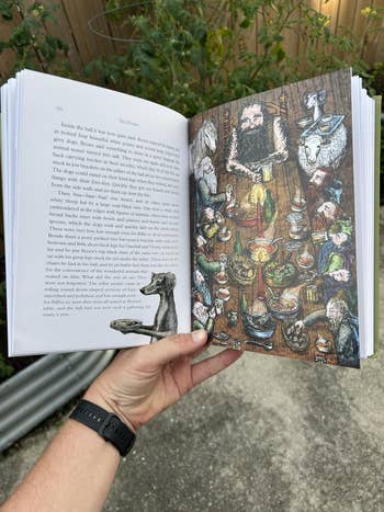 A idiosyncratic   holds an unfastened  illustrated publication  with a elaborate  drafting  of a mythical feast attended by assorted  creatures