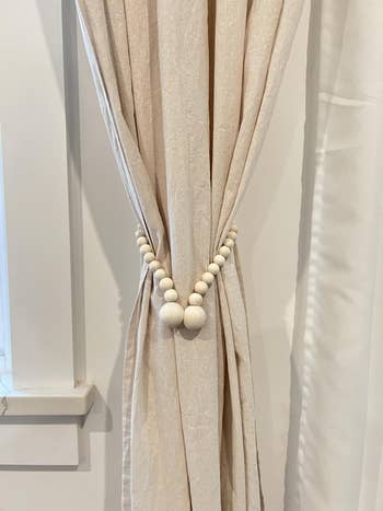 Curtain tied backmost with a drawstring of large, circular beads, showcasing a minimalist and elegant model attraction style