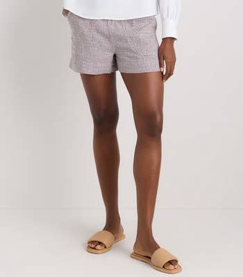 Person wearing checkered shorts and a achromatic long-sleeve top, paired with tan descent sandals