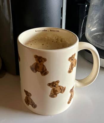 Mug with teddy carnivore  pattern, filled with frothy coffee. Top rim reads 