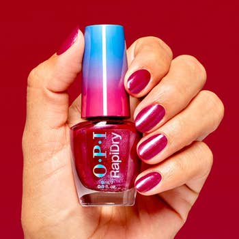 A manus  holding a vessel  of reddish  OPI nail polish