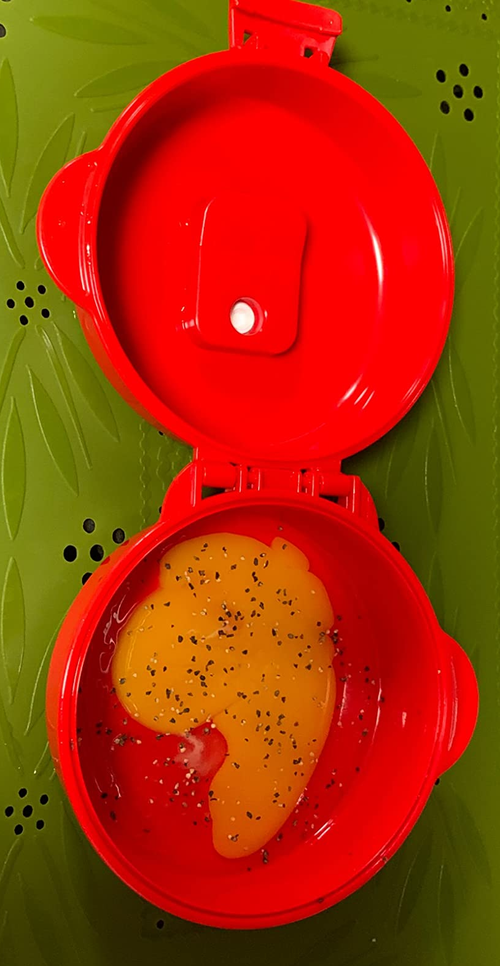 A microwavable egg cooker with a freshly cracked yolk inside