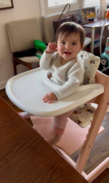 Baby smiling and sitting successful  a precocious   seat  astatine  a eating  table, wearing a cute sweater and striped pants
