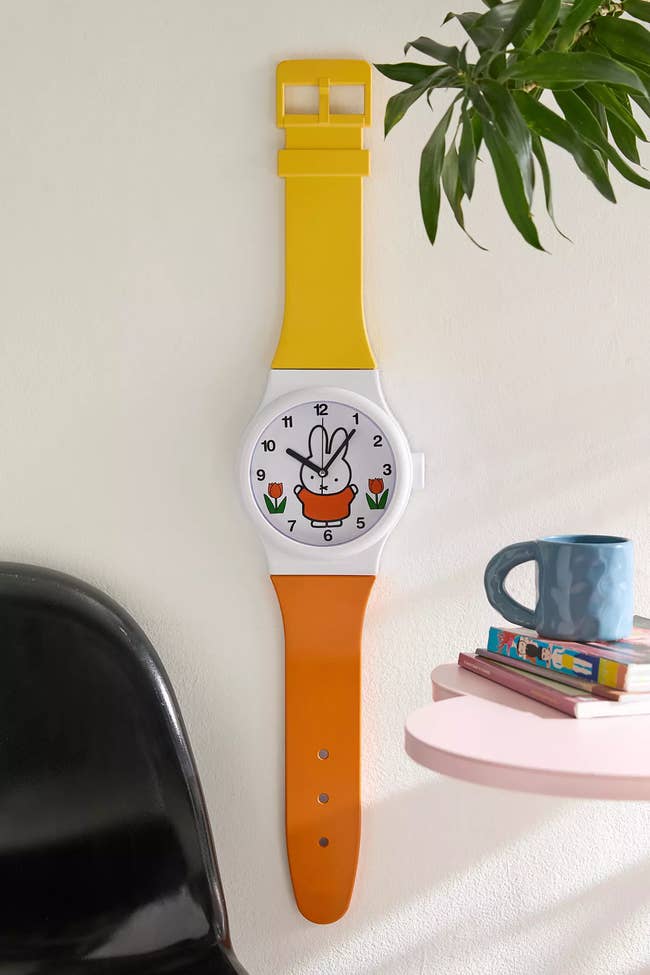 Large wall clock shaped like a wristwatch with a cartoon rabbit face; books and a mug are nearby