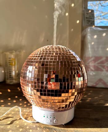 A rose gold disco ball-shaped humidifier releases mist on a table