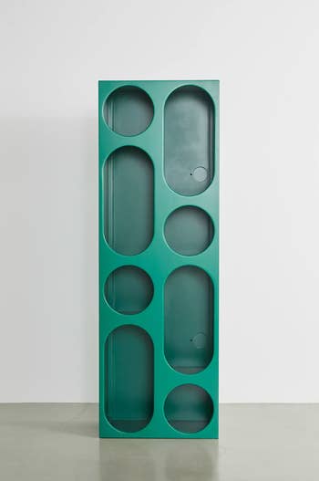 Tall green storage unit with circular openings, standing on a gray floor against a white wall. Ideal for modern home decor and organization