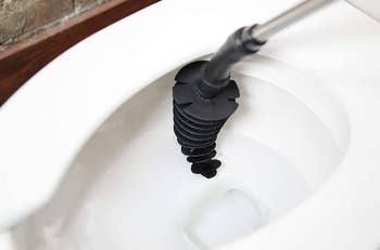 the black conical toilet plunger curving against the side of a toilet bowl