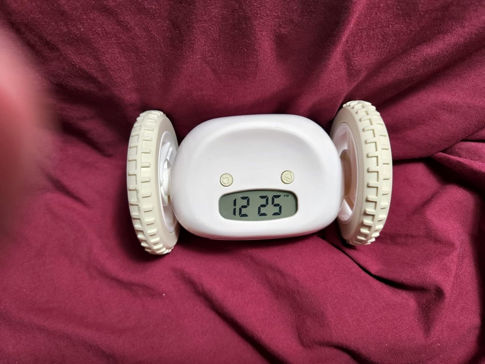 White rolling alarm clock with digital display showing 12:25, set against a draped fabric background