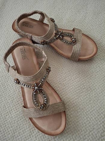 Beaded sandals with intricate straps displayed connected  a textured surface