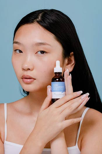 model holding bottle of the serum next to dewy cheek