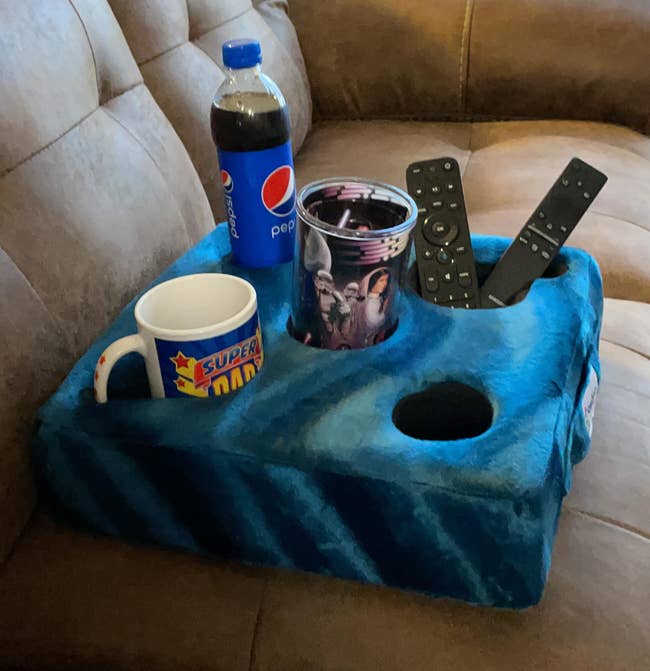 blue cup caddy holding a cup, pepsi bottle, coffee cup and two remotes