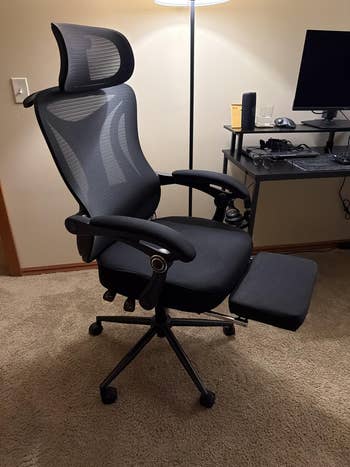 Ergonomic office chair with mesh backrest and adjustable headrest in a home office setting. Features extendable footrest for added comfort