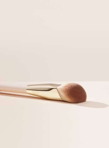 Makeup brush with a gold handle and soft bristles, placed on a light surface, ideal for applying cosmetics