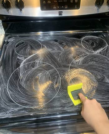 reviewer cleaning their stovetop utilizing the cleaning kit