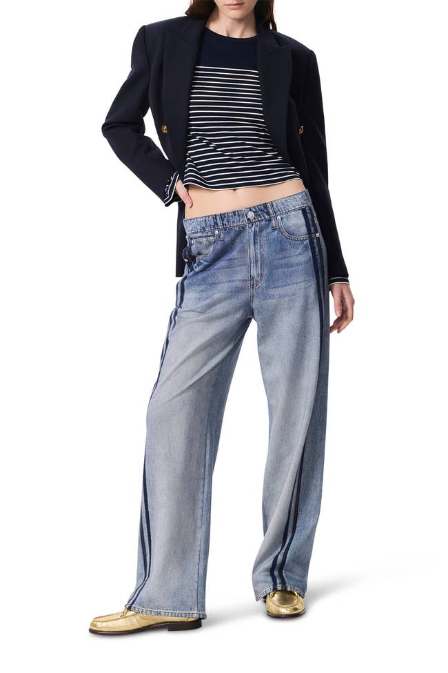 Person wearing a navy blazer, striped shirt, wide-leg jeans, and golden shoes, showcasing a stylish casual outfit
