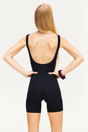 model in a black sleeveless jumpsuit posing with hands on hips, viewed from the back