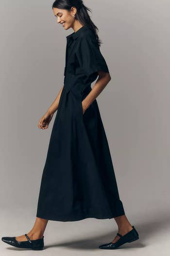 Model in a sleek, knee-length black dress with short sleeves and ballet flats, walking confidently