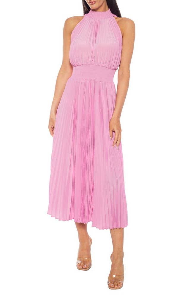 Model wearing a sleeveless pleated dress with a high neckline and ankle-strap heels, suitable for formal occasions