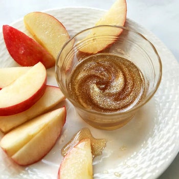 a ramekin full of glittery maple syrup on a plate with apple slices
