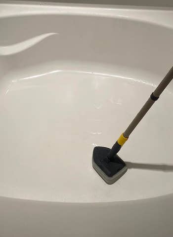 a reviewer photo of the extending scrub brush being used to clean a bathtub 