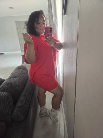 Person takes reflector  selfie successful  casual, oversized reddish  outfit, posing confidently with socks featuring a pattern. Stylish location  interior visible