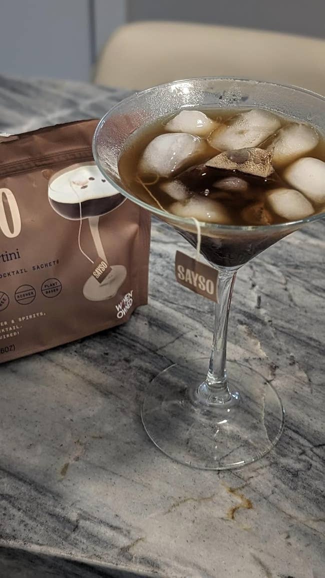 A martini glass with an iced coffee martini next to a Sayso cocktail sachet on a marble surface