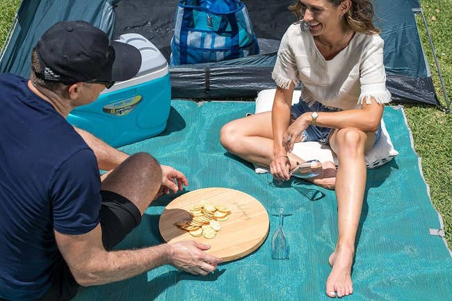 Two people sitting on a sand-sifting mat outdoors