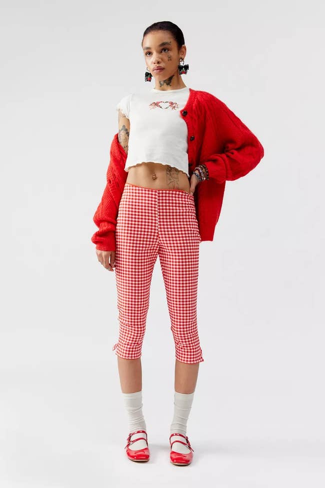 Model in a red cardigan, cropped white top, and checkered pants posing for a shopping article