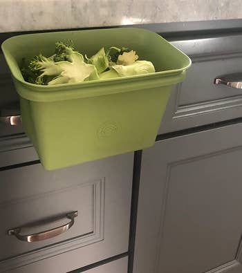 reviewer photo of the green bin attached to the side of a kitchen counter, holding discarded broccoli scraps