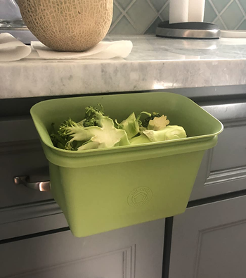 reviewer photo of the green bin attached to the side of a kitchen counter, holding discarded broccoli scraps