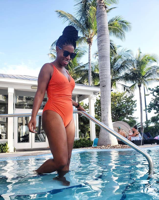 Reviewer in a stylish orange one-piece swimsuit by a poolside