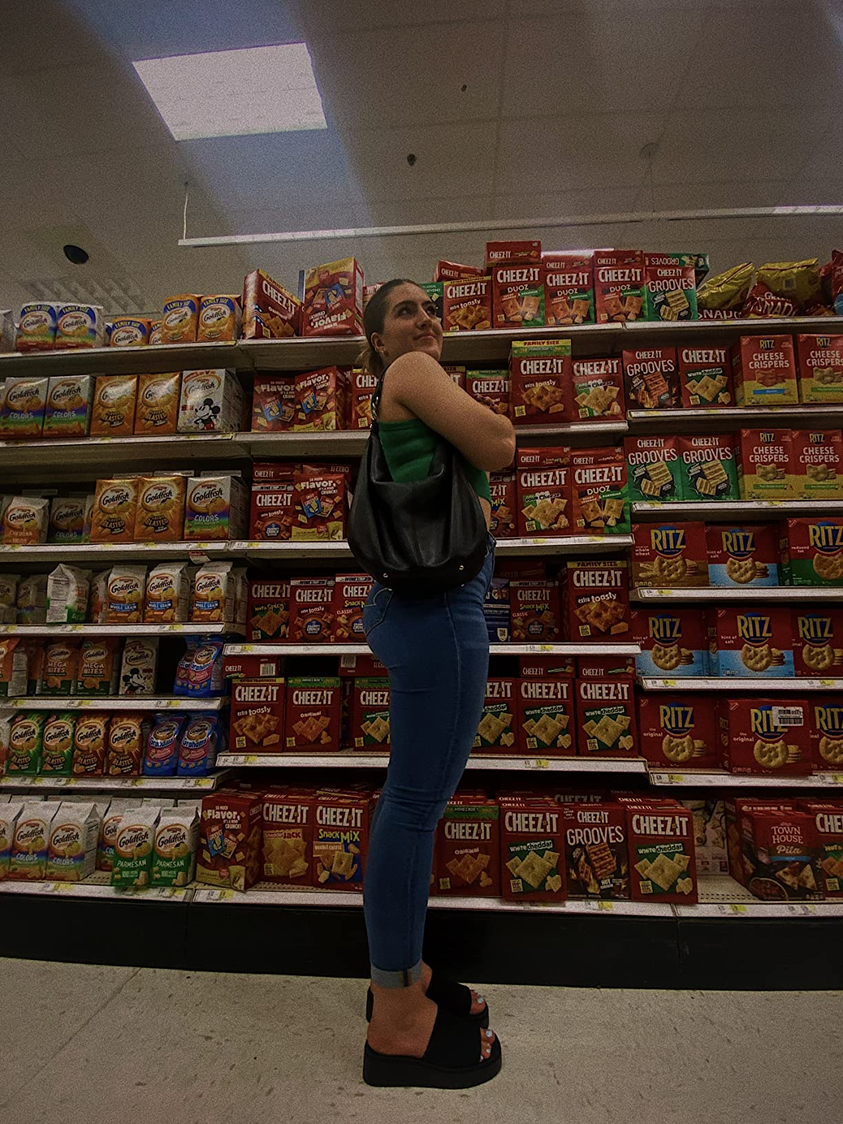 Person successful  a market  aisle holding a container  stands adjacent   shelves stocked with crackers and snacks