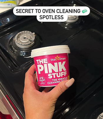 reviewer holding a tub of the pink stuff over their clean stove with text: secret to oven cleaning, spotless