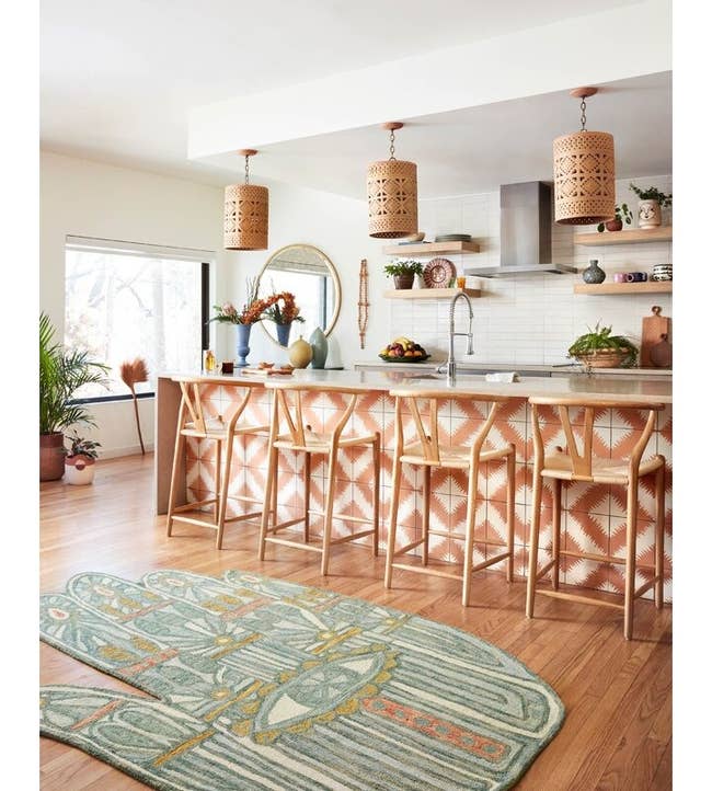 A modern kitchen with unique pendant lights, bar stools with geometric patterns, and a patterned rug