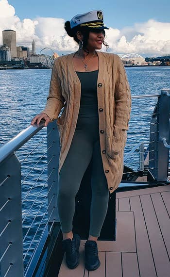 reviewer standing at a waterfront wearing the long khaki cable knit cardigan over a bodysuit