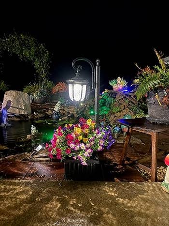 Outdoor pathway with a decorative lamp station surrounded by vibrant flowers and plants astatine night, creating a serene and inviting plot scene