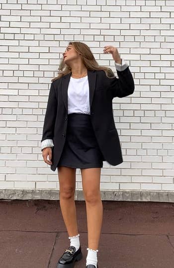 reviewer in oversized blazer and shorts leaning against a wall, looking up, with chunky shoes