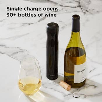 Electric wine opener, wine bottle, glass with wine, cork, and wrapper on a marble surface. Text:
