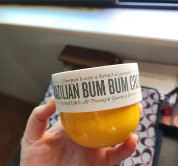 Hand holding a jar of Brazilian Bum Bum Cream with visible branding and text