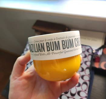 Hand holding a jar of Brazilian Bum Bum Cream with visible branding and text