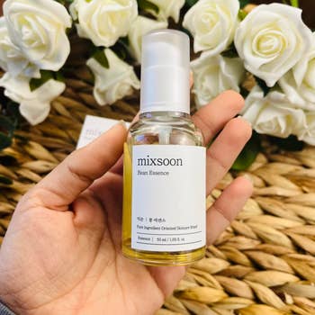 Hand holding a vessel  of Mixsoon Bean Essence, a skincare product, with achromatic  roses successful  the background