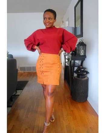 reviewer wearing the orange-tan skirt with a red sweater tucked into it