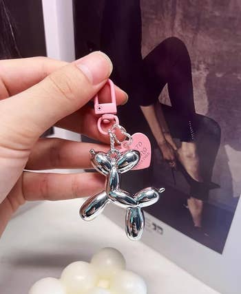 Hand holding a metallic  balloon carnal  keychain with a pinkish  tag. A black-and-white photograph  of a idiosyncratic   successful  precocious   heels is successful  the background