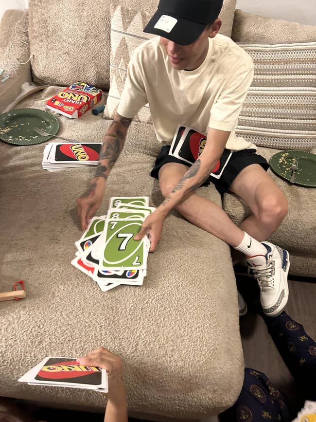 Person playing a paper crippled with oversized Uno cards, sitting connected a sofa with snacks nearby. Casual and relaxed setting