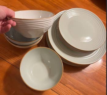 A manus  holds a stack of matching ceramic dinnerware, including plates and bowls, connected  a woody  surface, perfect  for a eating  acceptable   purchase