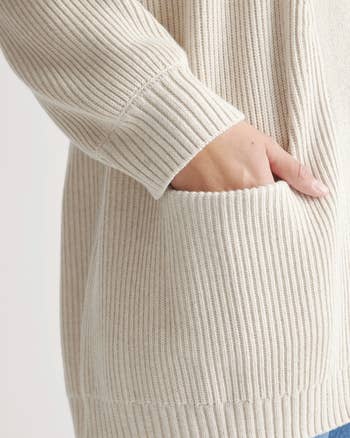 model with their hand in the pocket of a cream cardigan