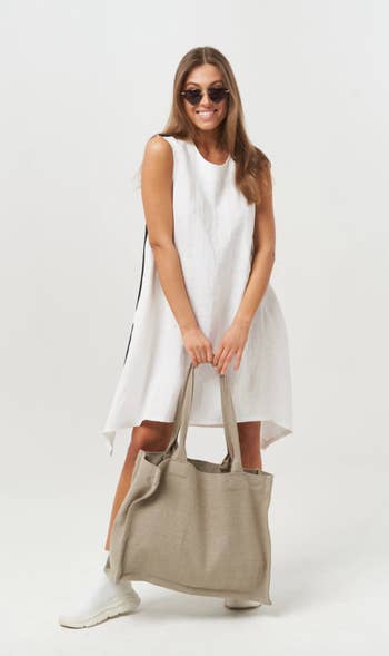 model wearing asymmetrical white tunic dress, holding tote bag