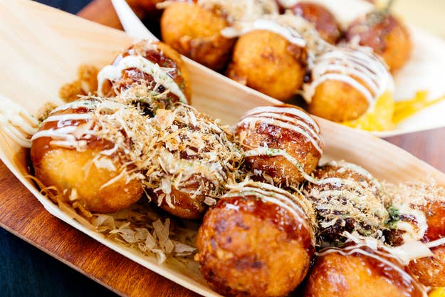 Takoyaki-Bällchen auf einem Tablett, garniert mit Sauce und Bonitoflocken, serviert in einem Holzteller