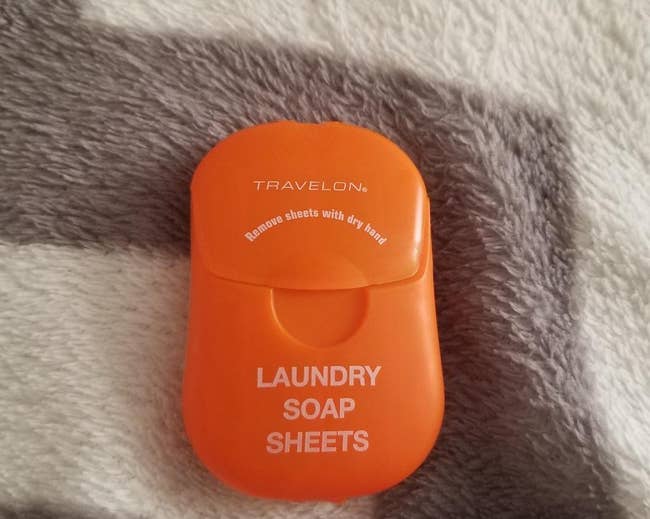 reviewer's orange pack of laundry soap sheets on top of a blanket